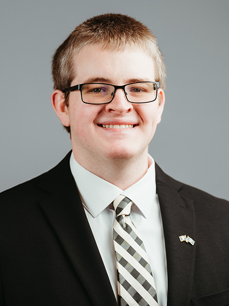 Marek Gibson wearing glasses, black suit coat with tie